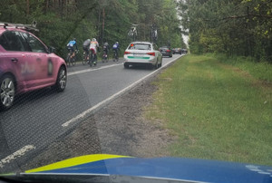 Na zdjęciu widoczny częściowo radiowóz oraz jadący zawodnicy wyścigu kolarskiego.