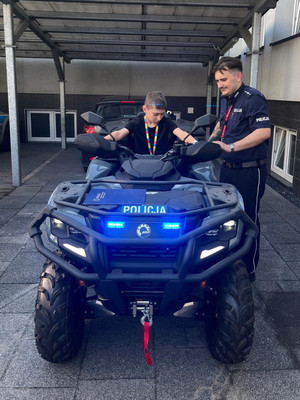 Na zdjęciu widoczny siedzący na quadzie chłopiec, obok niego stoi policjant.