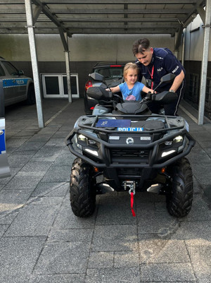 Na zdjęciu widoczna dziewczynka, która siedzi na quadzie. Obok niej widoczny policjant.