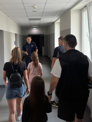 Na zdjęciu widoczny policjant, który prowadzi korytarzem dzieci i opiekunów.