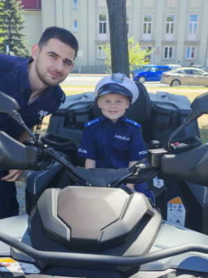 Na zdjęciu widoczny policjant oraz chłopiec w stroju policjanta, siedzący na motocyklu.