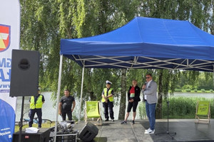 Na zdjęciu widoczna scena oraz przemawiający z niej mężczyzna i stojąca również na niej policjantka z wydziału ruchu drogowego.