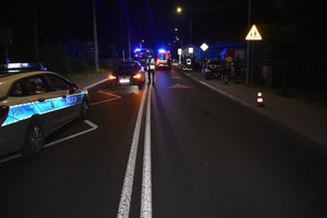 Na zdjęciu widoczne miejsce zdarzenia drogowego - policjant wykonujący czynności, ambulans i wóz strażacki.