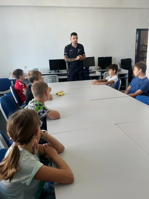 Na zdjęciu widoczny umundurowany policjant, który prowadzi pogadankę dla dzieci.