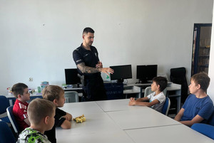 Na zdjęciu widoczny umundurowany policjant, który prowadzi pogadankę dla dzieci.