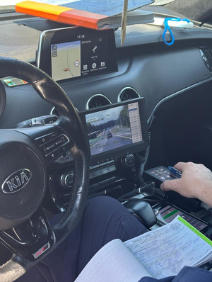 Na zdjęciu widoczny częściowo policjant wewnątrz radiowozu, trzymający wypisany mandat.