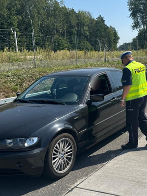 Na zdjęciu widoczny policjant przy samochodzie podczas kontroli drogowej.