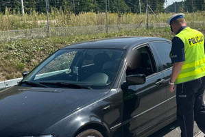 Na zdjęciu widoczny policjant stojący przy aucie podczas kontroli drogowej.