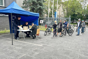 Na zdjęciu widoczni policjanci, którzy przyjmują dokumentację od mężczyzny, związaną ze znakowaniem roweru. Widoczne też inne osoby z rowerami, czekające w kolejce.