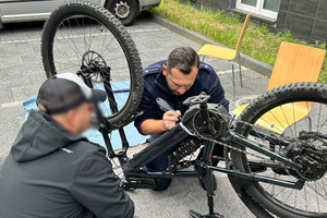 Na zdjęciu widoczny policjant, który znakuje rower. Obok widoczny kucający przy rowerze mężczyzna.