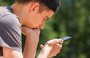 Na zdjęciu widoczny chłopiec patrzący na telefon, który trzyma w ręku.