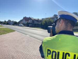 Na zdjęciu widoczny policjant, który wykonuje pomiar prędkości pojazdu.