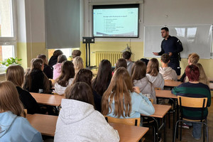 Na zdjęciu widoczny policjant, podczas prelekcji dla uczniów, którzy siedzą w ławkach.