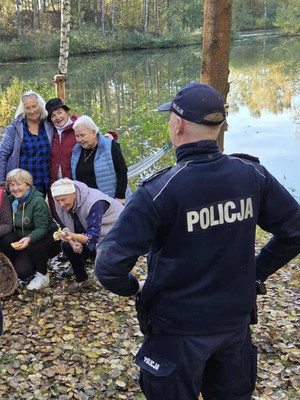 Na zdjęciu widoczny policjant na spotkaniu z seniorkami w lesie.