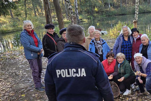 Na zdjęciu widoczny policjant na spotkaniu z seniorkami w lesie.