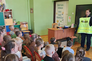 Na zdjęciu widoczna policjantka na spotkaniu z dziećmi. Policjantka pokazuje kamizelkę odblaskową.