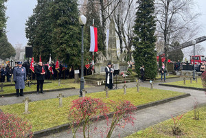Na zdjęciu widoczny Pomnik Niepodległości na cmentarzu oraz stojąca przed nim warta oraz ksiądz przy mikrofonie.