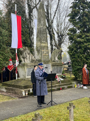 Na zdjęciu widoczny przed Pomnikiem Niepodległości policjant przy mikrofonie.