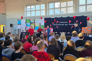 Na zdjęciu widoczna sala gimnastyczna oraz zebrani na niej uczniowie, policjant i grono pedagogiczne.