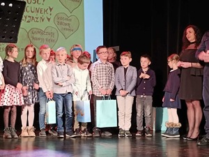 Na zdjęciu widoczna na scenie dzieci. Część z nich trzyma papierowe torby z nagrodami.