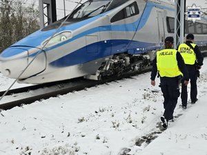 Patrol składający się z policjanta i funkcjonariusz Straży Ochrony Kolei sprawdzają rejon torowiska. Obok przejeżdża pendolino.