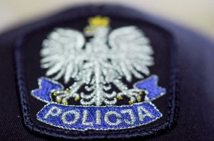 Na zdjęciu widoczna naszywka na policyjnej czapce, przedstawiająca orła w koronie, pod którym na niebieskiej wstędze widnieje napis: Policja.