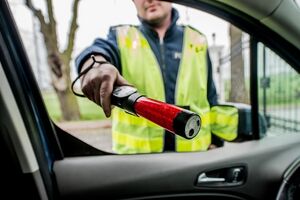 Na zdjęciu widoczny policjant, który w stronę kierowcy wyciąga alcoblow - urządzenie do badania stanu trzeźwości.
