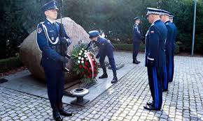 Na zdjęciu widoczni policjanci składający kwiaty przed pomnikiem i oddający hołd.