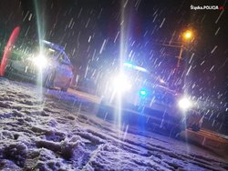 Na zdjęciu widoczny radiowóz i inny samochód na drodze podczas opadu śniegu.