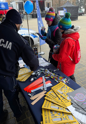 Na zdjęciu widoczny umundurowany policjant oraz dwie osoby przy stoisku profilaktycznym.