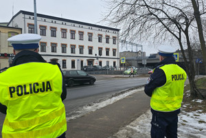 Na zdjęciu widoczni dwaj policjanci drogówki, którzy obserwują rejon przejścia dla pieszych.