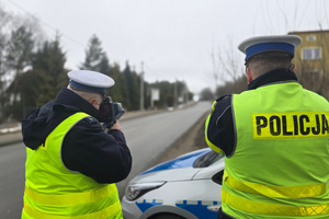 Na zdjęciu widoczni dwaj policjanci drogówki. Jeden z nich mierzy prędkość pojazdu.