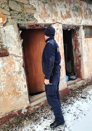 Na zdjęciu widoczny policjant, który idzie w stronę pustostanu.