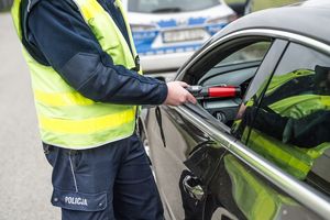 Na zdjęciu widoczny częściowo policjant, który sprawdza stan trzeźwości kierującego autem.