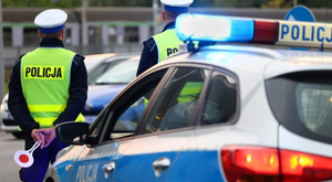 Na zdjęciu widoczni dwaj umundurowani policjanci przy radiowozie.