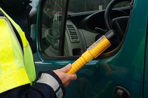 Na zdjęciu widoczny częściowo policjant, który kieruje w stronę kierowcy urządzenie do kontroli stanu trzeźwości.
