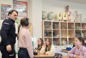 Na zdjęciu widoczny umundurowany policjant na spotkaniu z uczniami. Obok niego stoi uczennica.