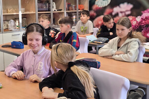Na zdjęciu widoczni uczniowie siedzący w ławkach. Jedna z uczennic przymierza policyjne słuchawki.