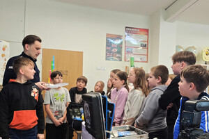 Na zdjęciu widoczny umundurowany policjant, który przedstawia sprzęt ratunkowy uczniom, stojącym wokół niego.