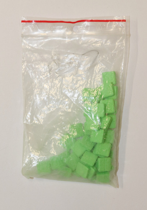Na zdjęciu widoczne zielone kwadratowe tabletki w woreczku strunowym.