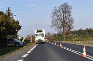Na zdjęciu widoczne miejsce wypadku drogowego. Na jezdni stoi biały samochód ciężarowy. Po lewej stronie radiowóz.