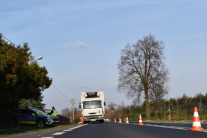Na zdjęciu widoczne miejsce wypadku drogowego. Na jezdni stoi biały samochód ciężarowy. Po lewej stronie radiowóz.