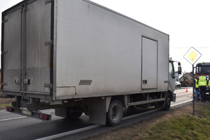 Na zdjęciu widoczny biały samochód ciężarowy na jezdni. Po prawej stronie widoczni policjanci.