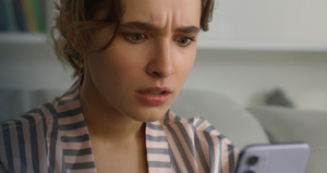 Na zdjęciu widoczna kobieta, patrząca na trzymany telefon komórkowy. Zdjęcie: cert.pl