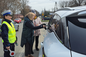 Osoby wręczają kierującemu ulotki. Obok nich stoi policjantka.