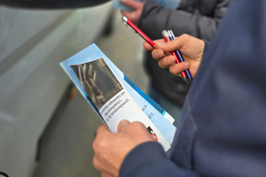 Ulotki i długopis trzymany w dłoniach.