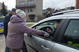 Osoby wręczają kierującemu ulotki.