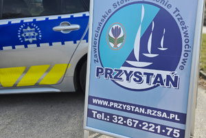 Tablica z danymi stowarzyszenia, za którą stoi radiowóz.