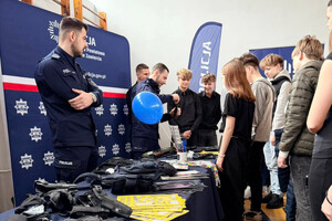 Policjanci przy stoisku profilaktycznym, prezentują uczniom policyjny sprzęt.