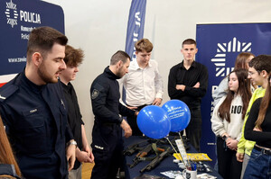 Policjanci przy stoisku profilaktycznym, prezentują uczniom policyjny sprzęt.